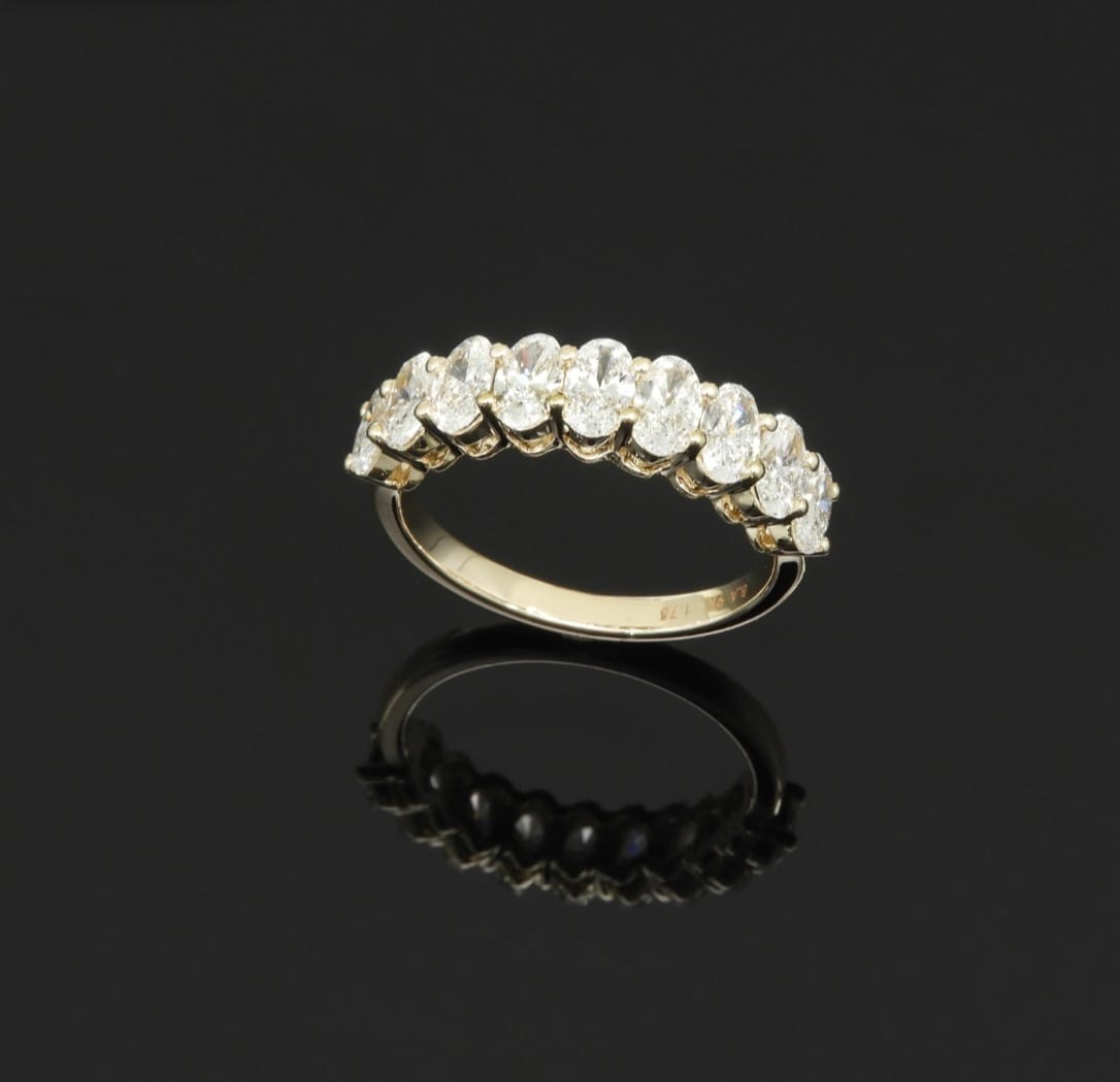 Nine oval-cut diamonds in a shared-prong half-eternity setting, on a polished yellow gold band.